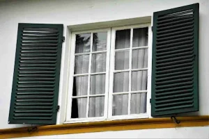 White-framed window with dark colonial shutters, showing classic styling in a Bahama vs Colonial shutters comparison.