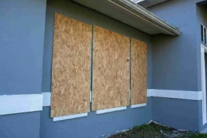 Home with plywood covering windows to block flying debris, demonstrating temporary hurricane shutter protection.