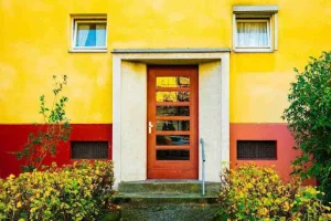 Modern home exterior with bold yellow and red facade highlighting current Front Door Trends in color, symmetry, and materials.