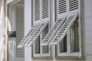 Exterior louvered hurricane shutters mounted on windows, designed to provide ventilation and storm protection for coastal homes.