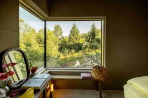 A quiet reading nook with a corner fixed window overlooking a garden, designed with picture windows