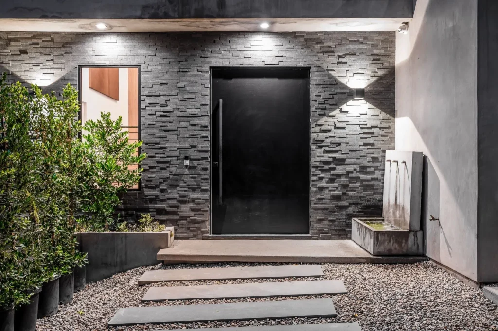 Modern black entry door in a stone facade illustrating fiberglass vs steel front door styles for Florida homes